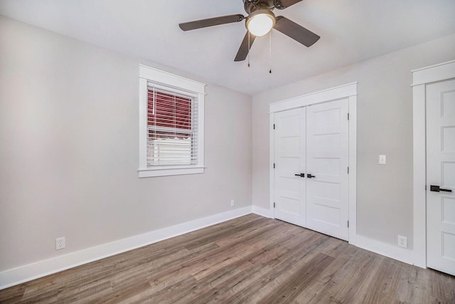 unfurnished bedroom featuring a closet, baseboards, a ceiling fan, and wood finished floors