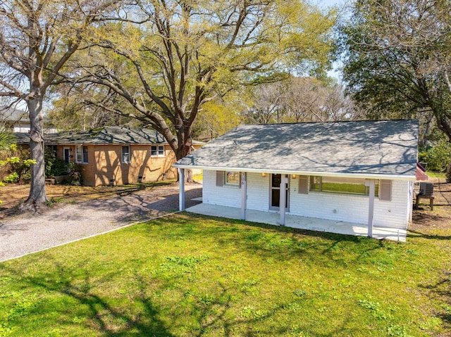 view of front of home featuring a shingled roof, aphalt driveway, brick siding, a front yard, and covered porch