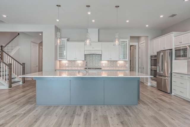 kitchen with hanging light fixtures, black microwave, stainless steel fridge, a kitchen island with sink, and white cabinets