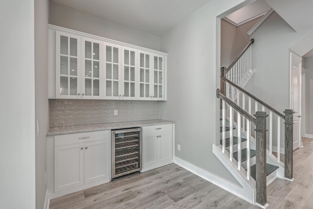 bar featuring white cabinets, light stone countertops, beverage cooler, and light wood-type flooring