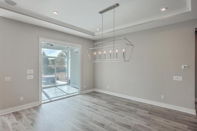 unfurnished dining area with a tray ceiling, light hardwood / wood-style floors, and a notable chandelier