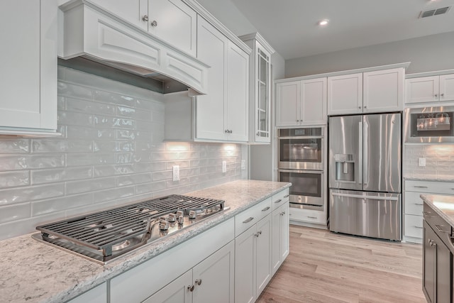 kitchen featuring premium range hood, tasteful backsplash, white cabinetry, light hardwood / wood-style floors, and stainless steel appliances