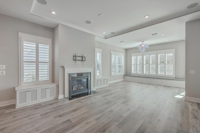 unfurnished living room with a healthy amount of sunlight, a high end fireplace, and light hardwood / wood-style floors