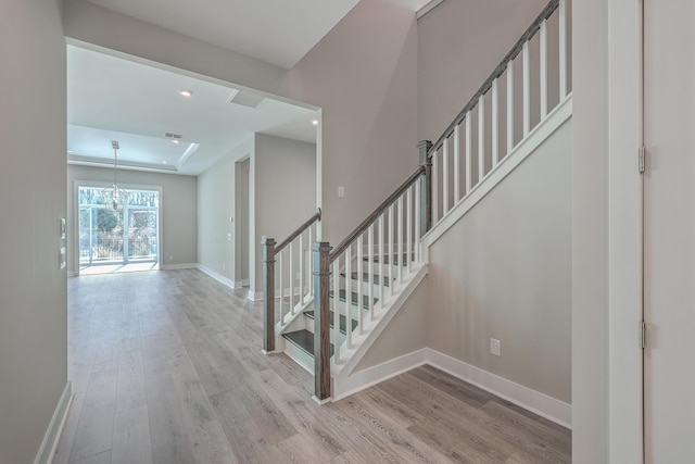 staircase featuring an inviting chandelier, wood-type flooring, and a tray ceiling