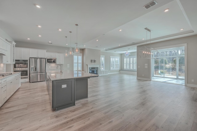 kitchen with a large island, appliances with stainless steel finishes, white cabinetry, hanging light fixtures, and backsplash