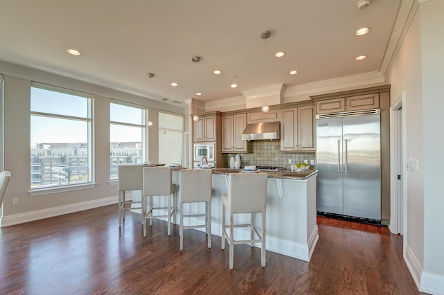 kitchen with light stone counters, backsplash, built in appliances, pendant lighting, and a kitchen island