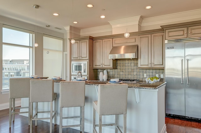 kitchen with pendant lighting, stone counters, exhaust hood, built in appliances, and decorative backsplash