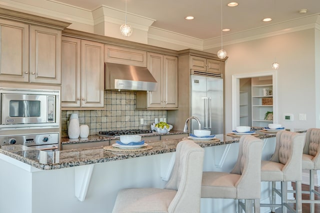 kitchen featuring pendant lighting, built in appliances, extractor fan, and dark stone countertops