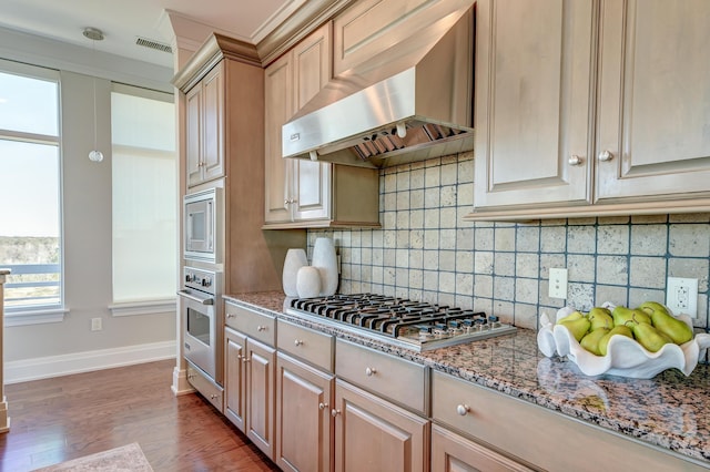 kitchen featuring light brown cabinets, light stone countertops, wall chimney range hood, and appliances with stainless steel finishes