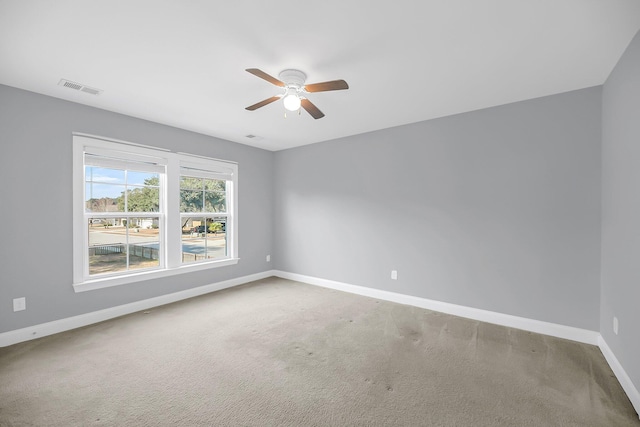 carpeted spare room featuring baseboards, visible vents, and ceiling fan