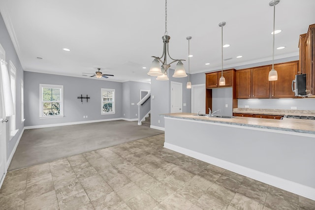 kitchen with a sink, baseboards, brown cabinetry, stainless steel microwave, and pendant lighting