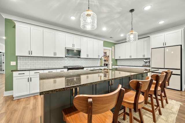 kitchen with light wood-type flooring, backsplash, stainless steel appliances, pendant lighting, and white cabinets