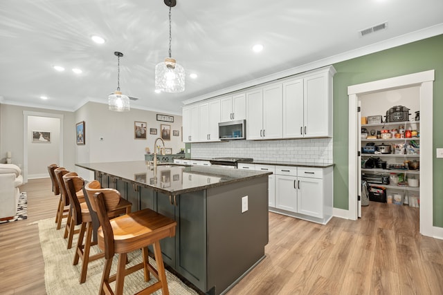 kitchen featuring appliances with stainless steel finishes, hanging light fixtures, white cabinets, dark stone countertops, and light hardwood / wood-style flooring