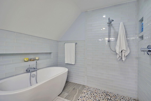 bathroom with a freestanding bath, vaulted ceiling, tile walls, and tiled shower