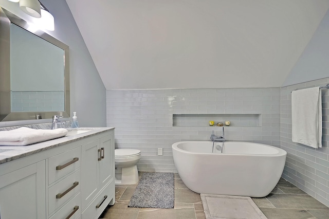 full bathroom featuring toilet, vanity, tile walls, vaulted ceiling, and a freestanding bath