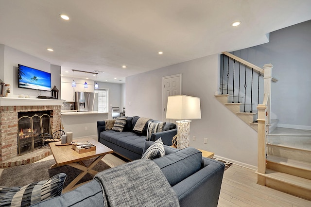 living room featuring light wood-style flooring, a fireplace, stairway, and baseboards