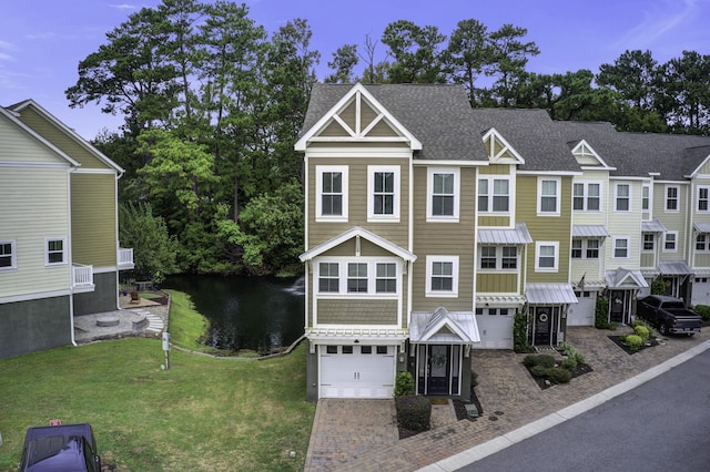 view of property featuring a standing seam roof, a water view, an attached garage, a shingled roof, and decorative driveway