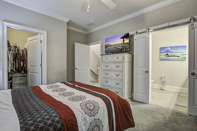 bedroom with a barn door, crown molding, a ceiling fan, a spacious closet, and carpet floors