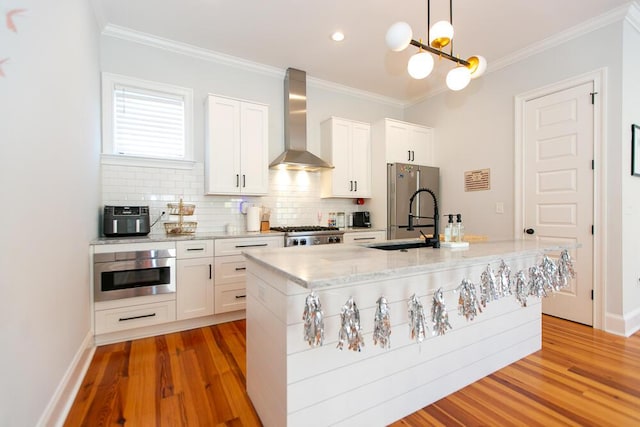 kitchen with white cabinetry, a kitchen island with sink, wall chimney range hood, and decorative light fixtures