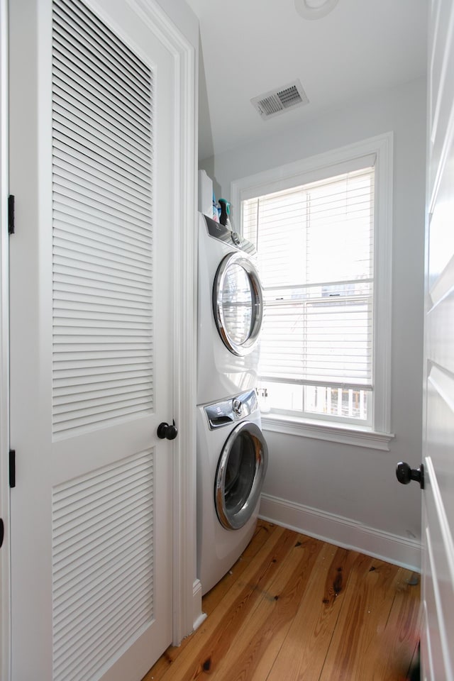 washroom with stacked washer / drying machine and light hardwood / wood-style flooring