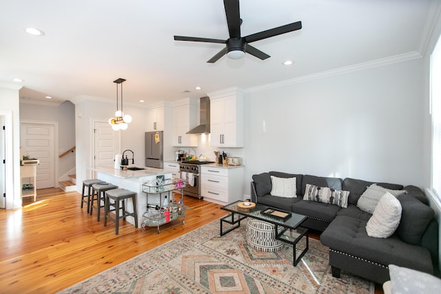 living room with crown molding, ceiling fan, sink, and light hardwood / wood-style flooring