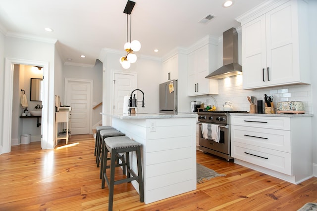 kitchen with an island with sink, appliances with stainless steel finishes, white cabinets, and wall chimney exhaust hood