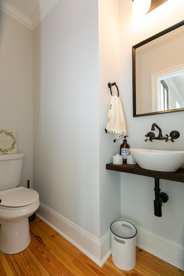 bathroom featuring hardwood / wood-style flooring, crown molding, sink, and toilet