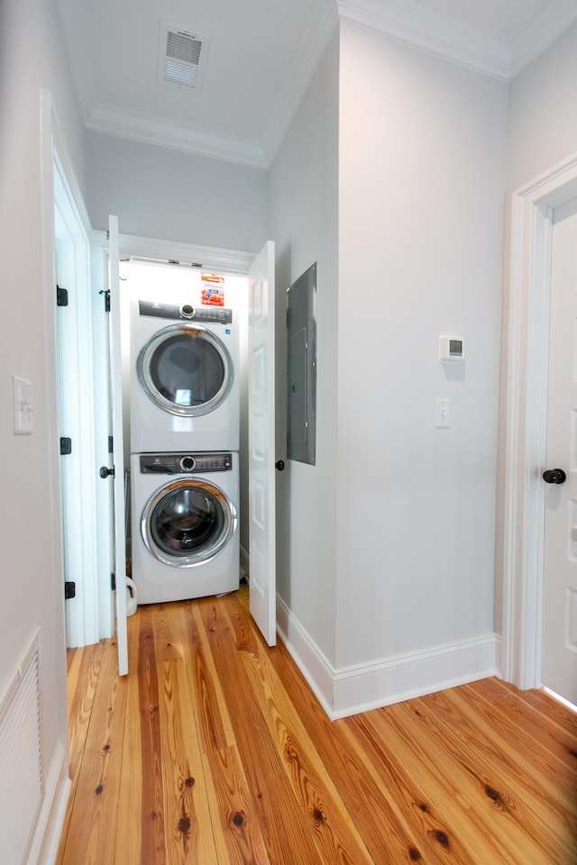 laundry area with ornamental molding, stacked washing maching and dryer, electric panel, and light hardwood / wood-style floors