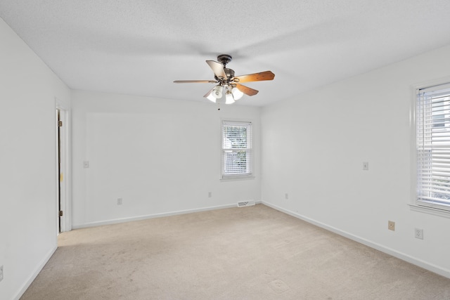 empty room featuring light carpet, ceiling fan, a healthy amount of sunlight, and a textured ceiling