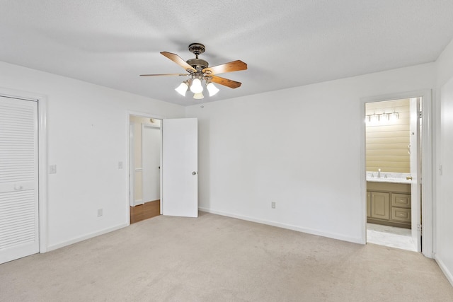 unfurnished bedroom featuring ensuite bath, ceiling fan, light colored carpet, a textured ceiling, and a closet