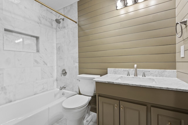 full bathroom featuring wood walls, vanity, tiled shower / bath combo, and toilet