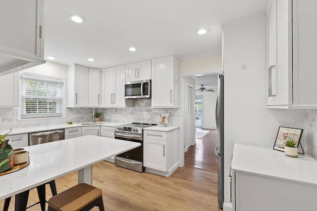 kitchen featuring backsplash, white cabinetry, stainless steel appliances, and light hardwood / wood-style flooring