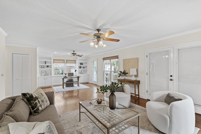 living room featuring french doors, built in features, light hardwood / wood-style floors, a textured ceiling, and ornamental molding