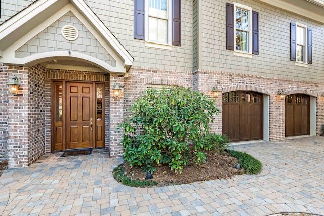 property entrance featuring a garage, decorative driveway, and brick siding