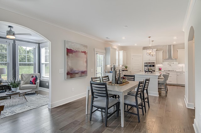 dining area featuring arched walkways, dark wood-type flooring, ornamental molding, baseboards, and ceiling fan with notable chandelier