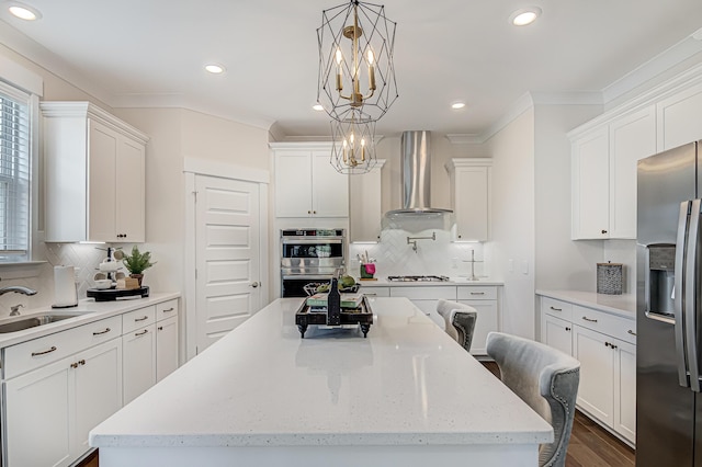 kitchen featuring wall chimney range hood, a sink, appliances with stainless steel finishes, and crown molding