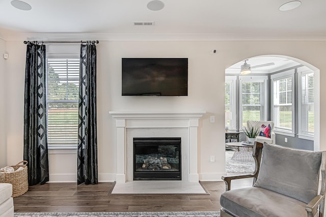 living room with a fireplace with flush hearth, ornamental molding, wood finished floors, and visible vents