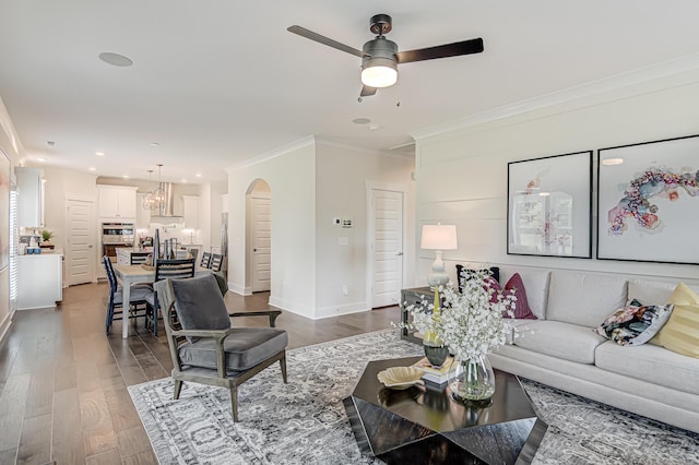 living area with baseboards, arched walkways, dark wood finished floors, ornamental molding, and ceiling fan with notable chandelier