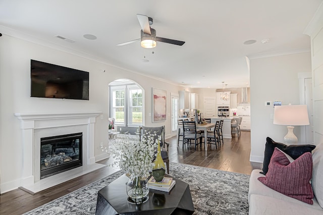 living room featuring visible vents, baseboards, dark wood-style floors, a glass covered fireplace, and crown molding