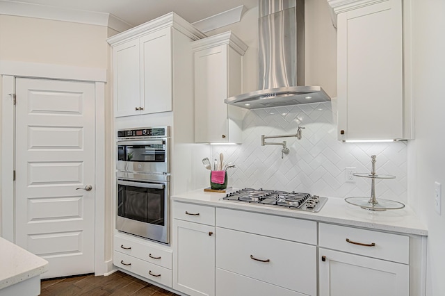 kitchen with dark wood-style flooring, white cabinetry, wall chimney range hood, appliances with stainless steel finishes, and decorative backsplash