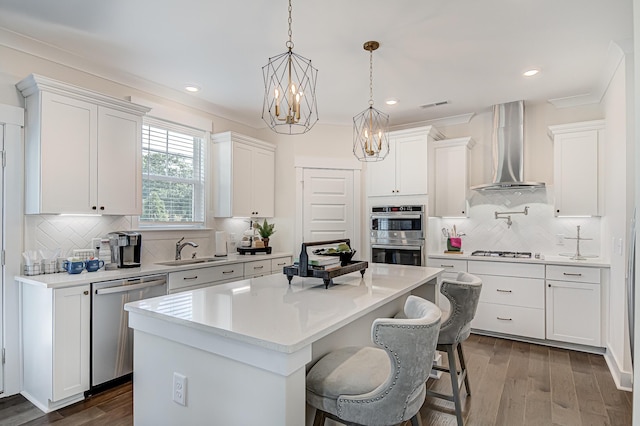 kitchen with a sink, a kitchen island, visible vents, appliances with stainless steel finishes, and wall chimney range hood