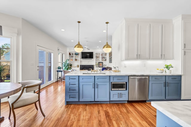 kitchen with light wood finished floors, open floor plan, light countertops, stainless steel appliances, and a sink