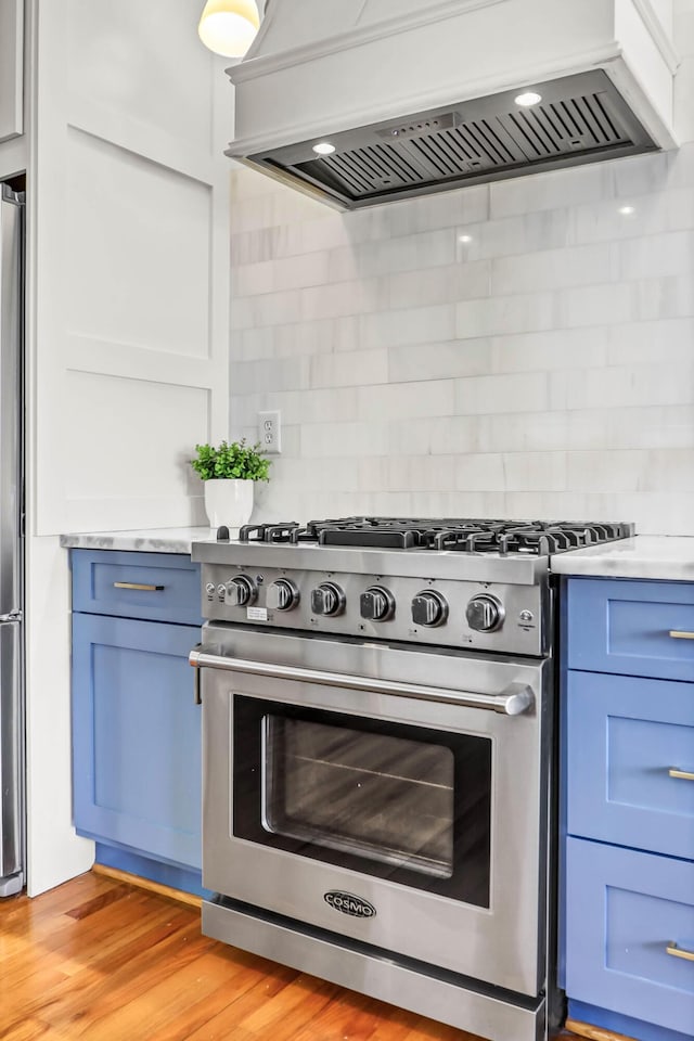 kitchen with blue cabinetry, light countertops, custom range hood, appliances with stainless steel finishes, and light wood-type flooring