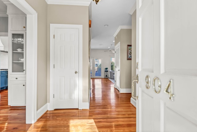 corridor featuring baseboards, crown molding, and light wood finished floors