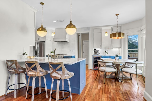 kitchen with stainless steel fridge with ice dispenser, wine cooler, a peninsula, custom exhaust hood, and light wood-style floors