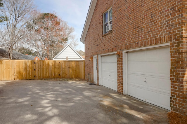 garage featuring concrete driveway, fence, and a gate