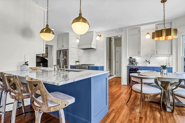 kitchen with light wood-style flooring, beverage cooler, a peninsula, premium range hood, and a breakfast bar