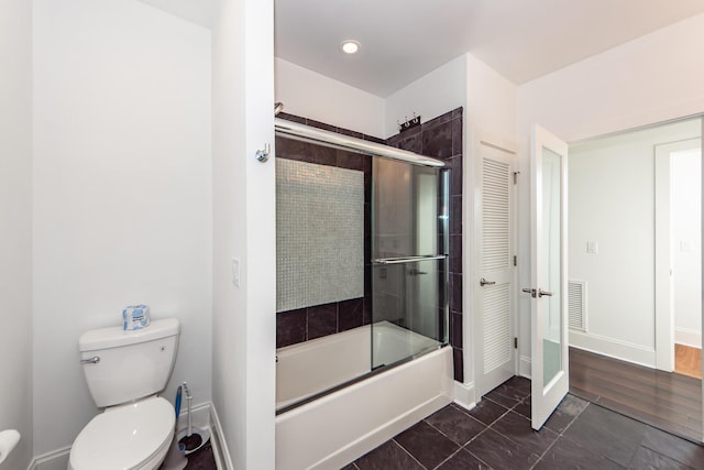 bathroom with hardwood / wood-style floors, toilet, and shower / bath combination with glass door