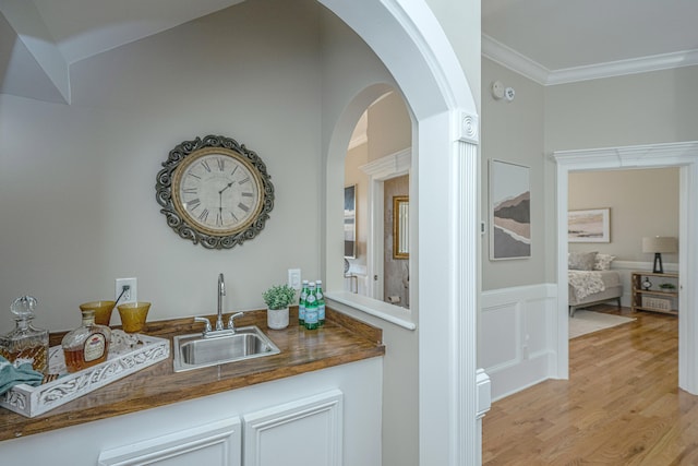 bar featuring light hardwood / wood-style floors, ornamental molding, and sink