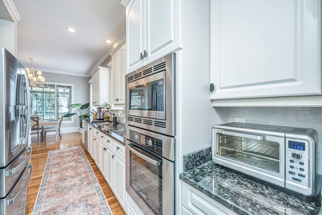 kitchen with decorative backsplash, white cabinets, an inviting chandelier, appliances with stainless steel finishes, and light hardwood / wood-style floors